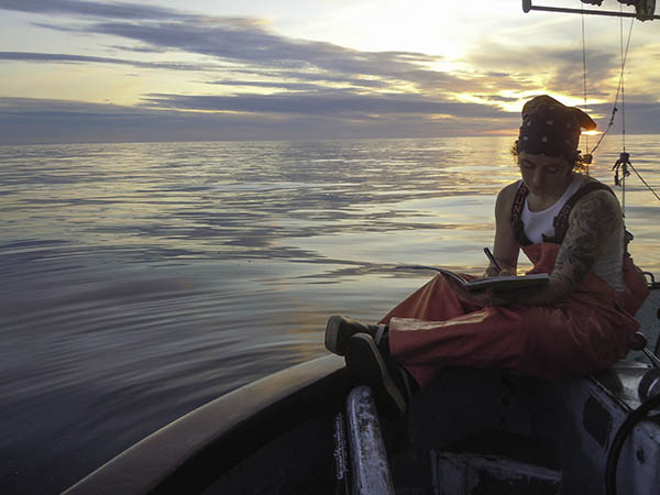 Tele Aadsen writing on anchor of the boat at sunset